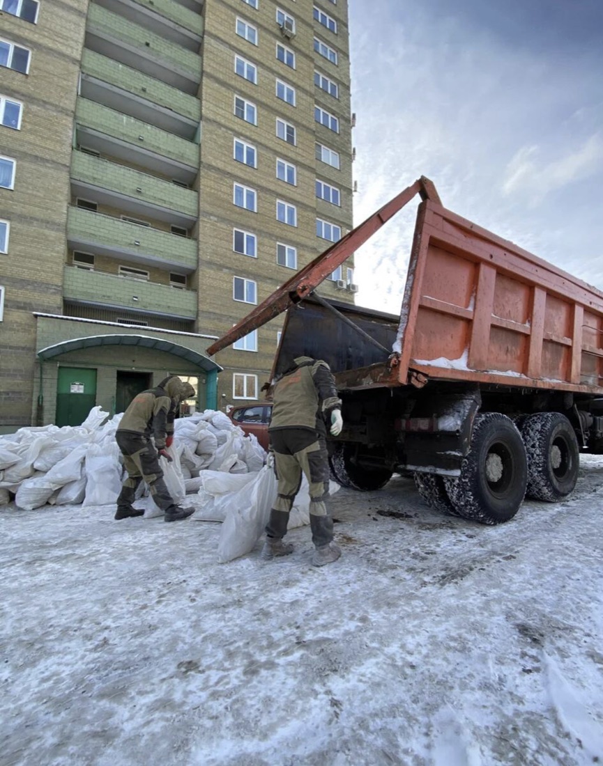 Бригада грузит мешки со строительным мусором в самосвал у дома